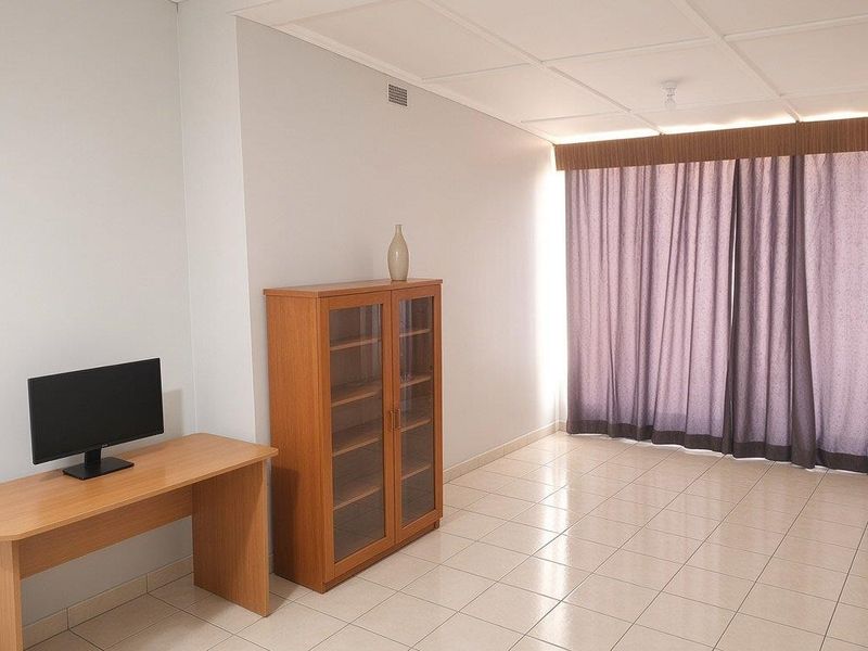 A neutrally painted living area featuring tiled flooring, a drop ceiling, and large window curtains.