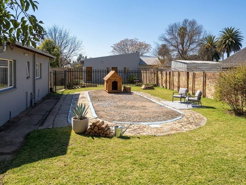 Rear garden area featuring a lawn, paved walkway, and a disused pool space currently filled with gravel, enclosed by brick and metal fencing.