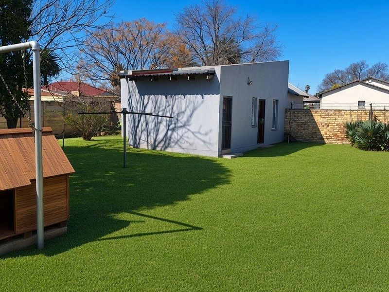 A well-maintained garden featuring artificial turf, a brick boundary wall, and a detached outbuilding suitable for storage or utility use.