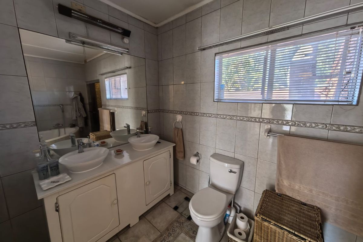 A functional bathroom featuring a double vanity with vessel sinks, large wall mirror, toilet, and neutral tiled finishes throughout.