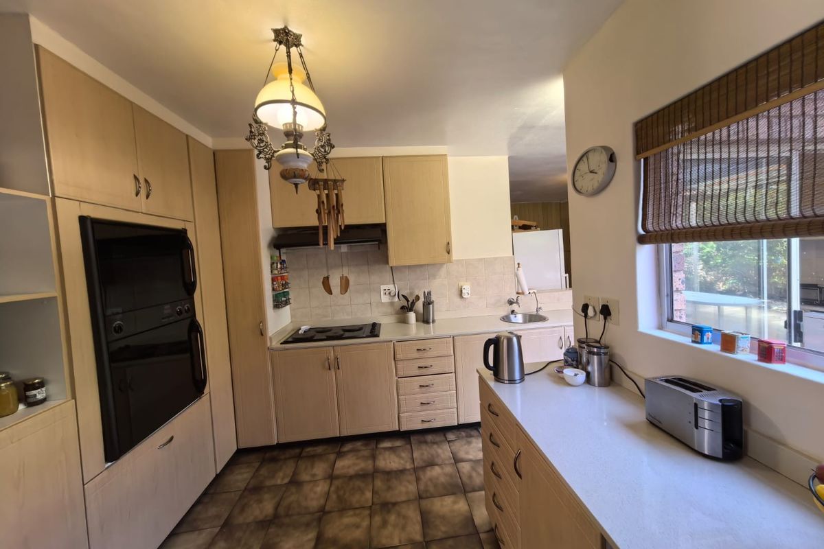 A functional kitchen featuring light wood cabinetry, stone countertops, built-in oven, electric hob, and tiled flooring with a view to the exterior.