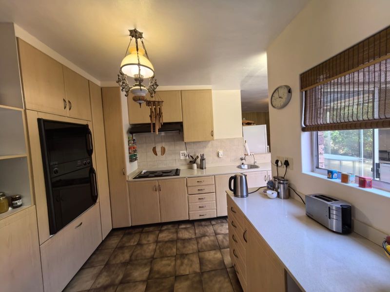 A functional kitchen featuring light wood cabinetry, stone countertops, built-in oven, electric hob, and tiled flooring with a view to the exterior.