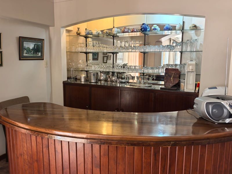 A dedicated home bar area featuring a curved wooden counter, mirrored back bar, and integrated glass shelving for display and storage.