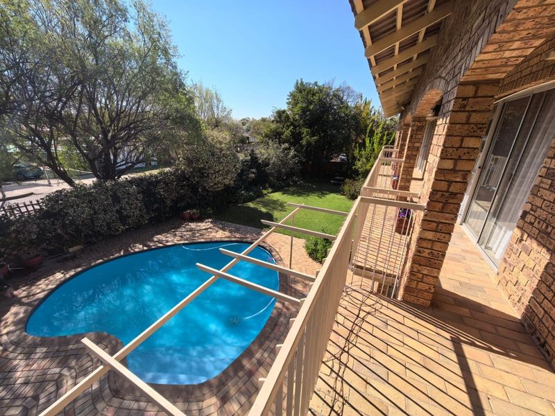 Elevated view of a backyard featuring a swimming pool, brick-paved patio area, and a balcony with metal railings overlooking the garden.