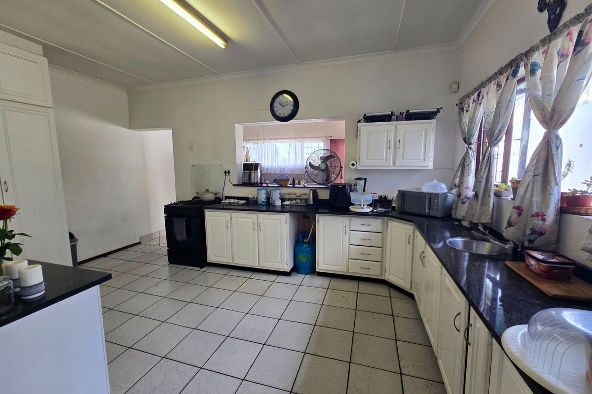A functional kitchen featuring white cabinetry, dark granite countertops, a freestanding stove, and tiled flooring with a serving hatch to the adjacent room.