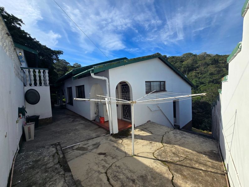 Rear exterior view of the property featuring a concrete paved area, security gate, and established surrounding greenery.