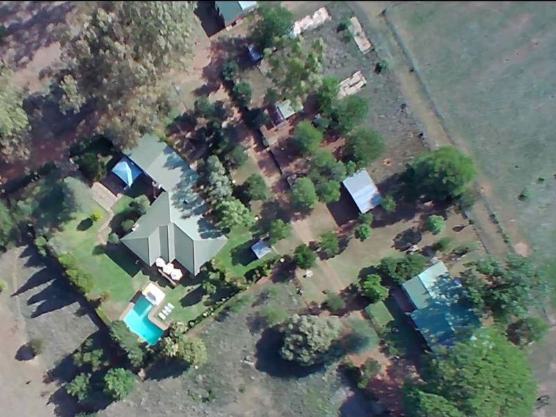 Aerial view of a farm property featuring a main residence with a swimming pool, multiple outbuildings, and surrounding landscaped grounds.