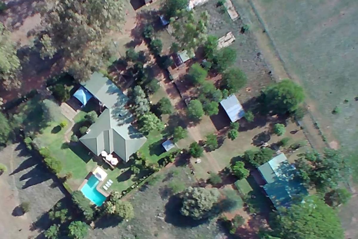 Aerial view of a farm property featuring a main residence with a swimming pool, multiple outbuildings, and surrounding landscaped grounds.