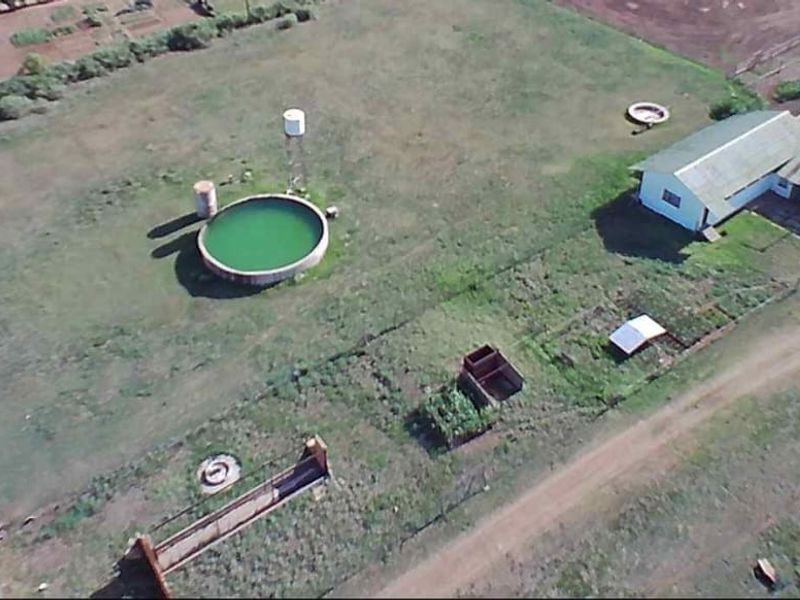 Aerial view of a farm property featuring a large water reservoir, storage tank, and existing farm buildings situated on expansive grounds.
