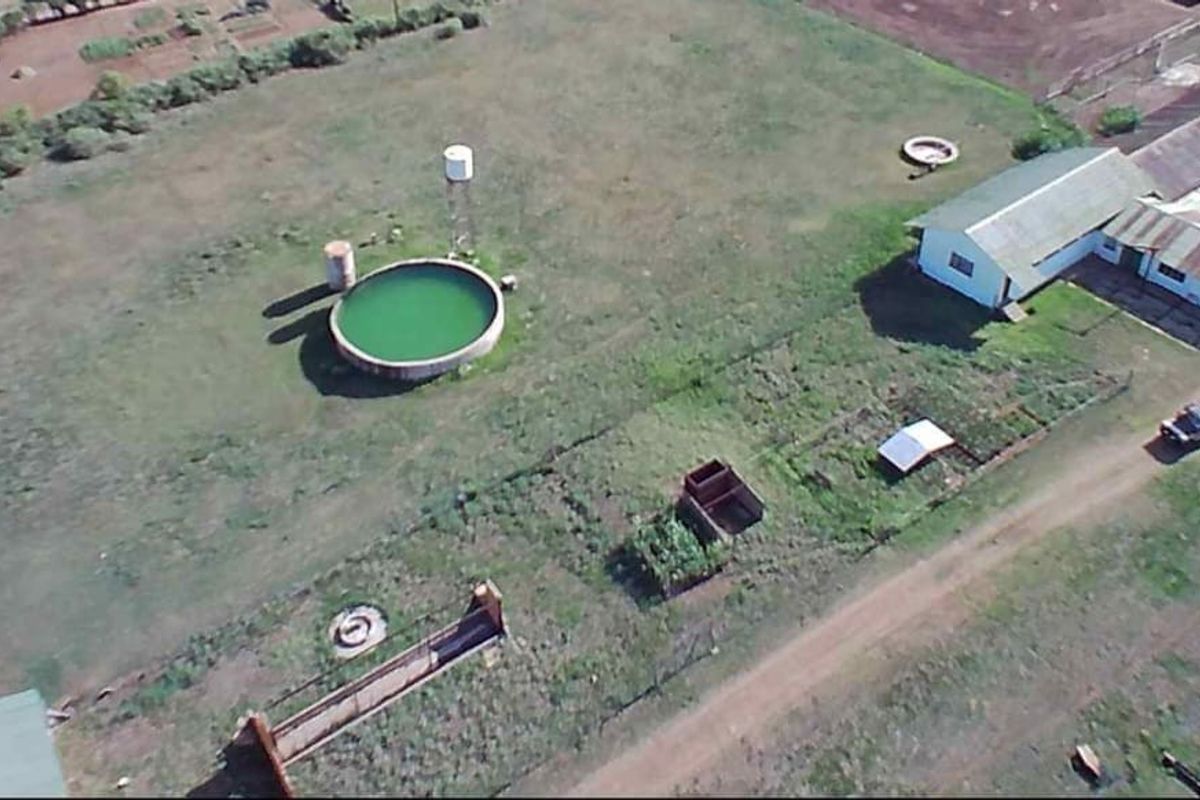 Aerial view of a farm property featuring a large water reservoir, storage tank, and existing farm buildings situated on expansive grounds.