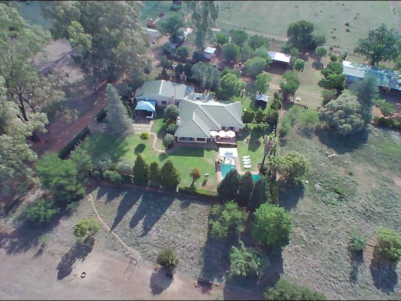 Aerial view of a farm property featuring a main residence, swimming pool, landscaped gardens, and surrounding rural land.