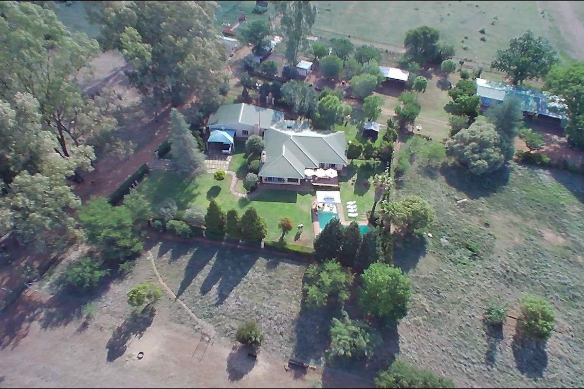 Aerial view of a farm property featuring a main residence, swimming pool, landscaped gardens, and surrounding rural land.