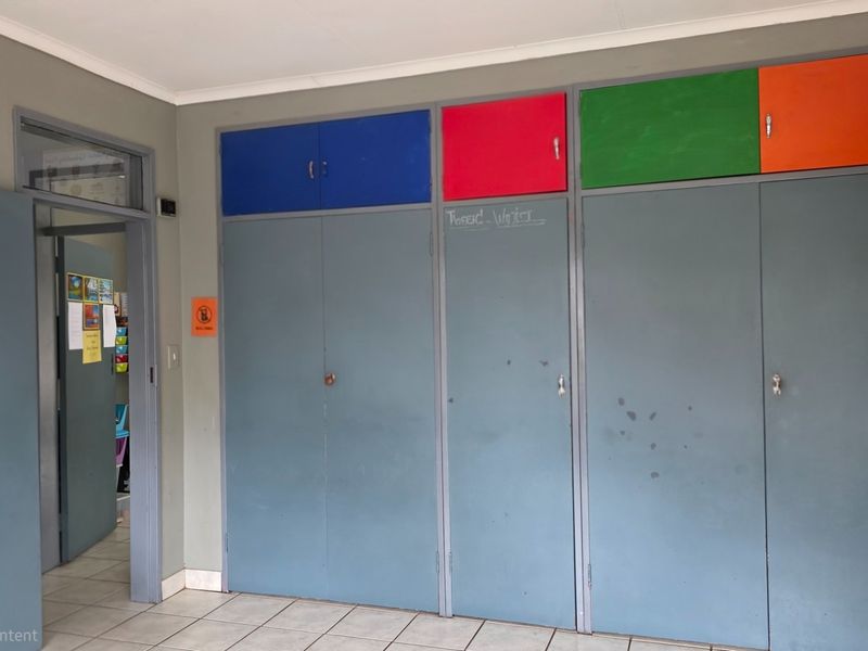 A functional hallway area featuring extensive built-in storage cupboards with multi-colored overhead cabinets and neutral tiled flooring.