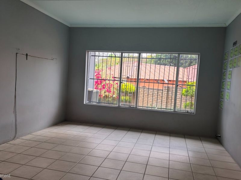 An empty living room featuring tiled flooring and a large window with security bars, requiring minor cosmetic updates to the walls.