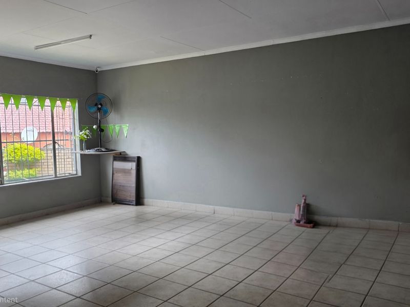 A spacious, empty living area featuring neutral tiled flooring and large windows with security bars, offering a blank canvas for interior design.