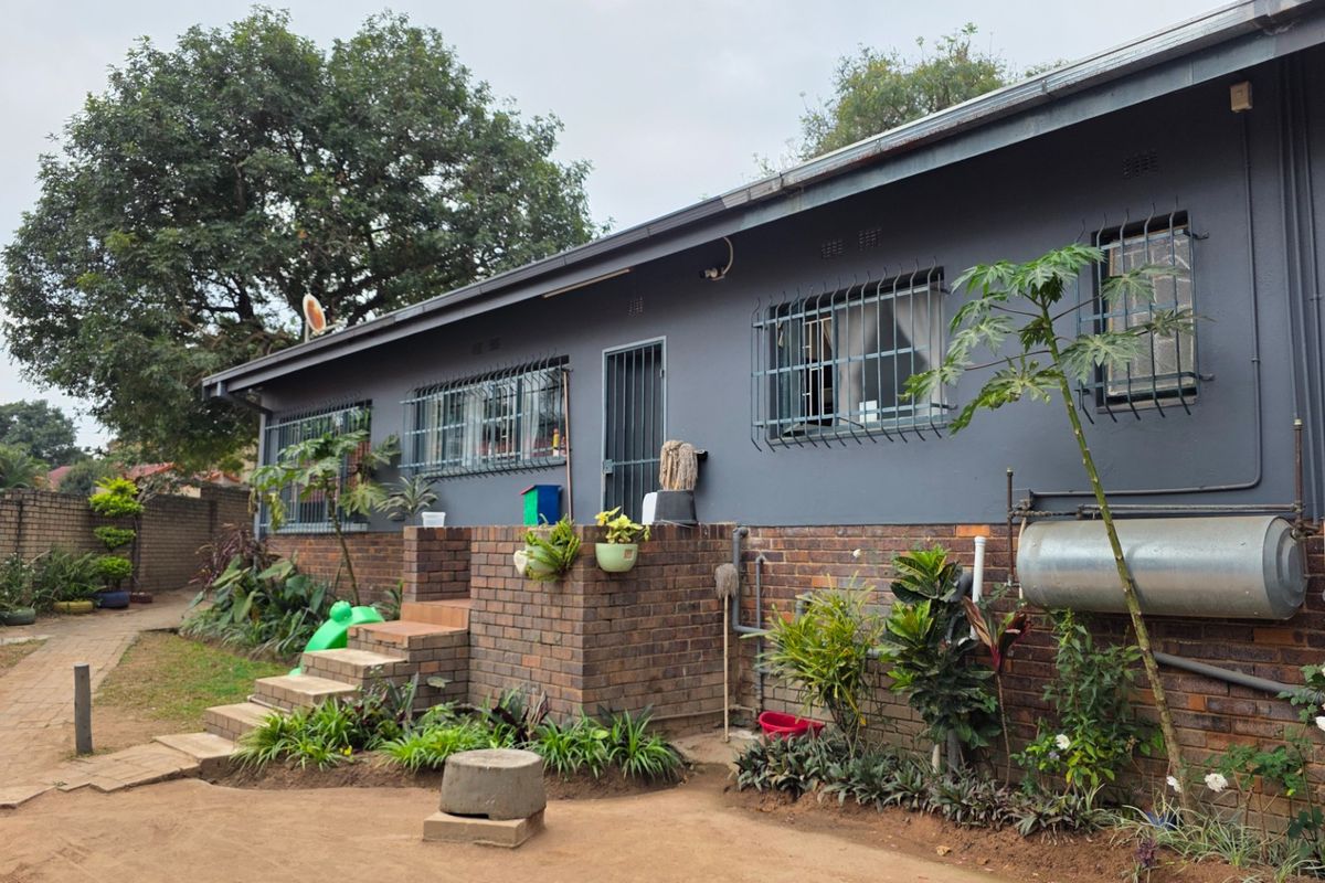 Rear view of the house featuring a brick and painted facade, security bars on windows, external geyser, and a paved garden walkway.