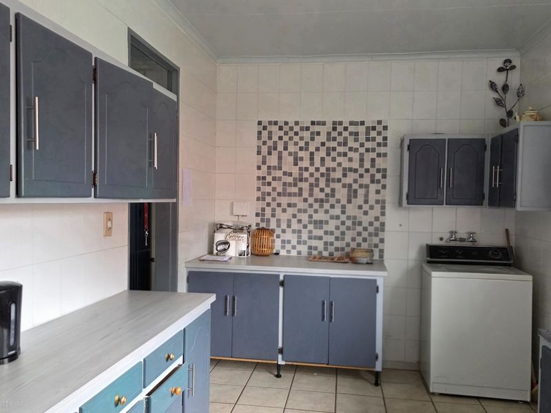 A functional kitchen featuring built-in cabinetry, tiled splashbacks, and tiled flooring, offering a practical layout with potential for modern cosmetic updates.