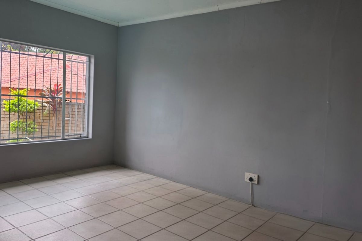 An empty bedroom featuring tiled flooring, grey painted walls, and a window fitted with security bars.