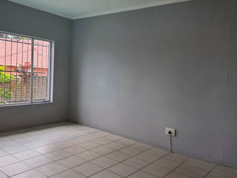 An empty bedroom featuring tiled flooring, grey painted walls, and a window fitted with security bars.