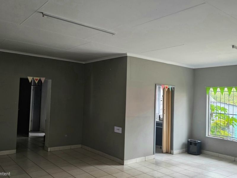An empty living area featuring tiled flooring, neutral grey walls, and a window with security bars, offering a blank canvas for interior design.