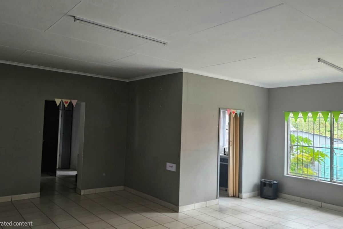An empty living area featuring tiled flooring, neutral grey walls, and a window with security bars, offering a blank canvas for interior design.