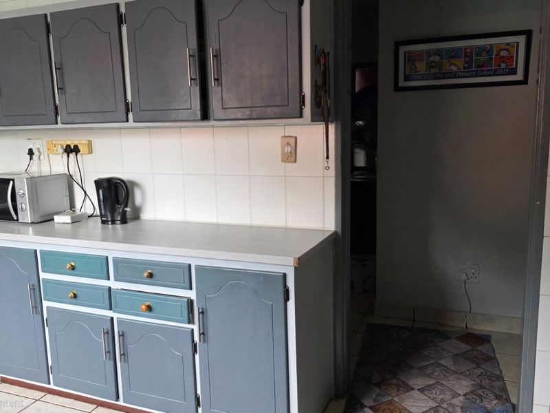 A functional kitchen featuring grey built-in cabinetry, a tiled backsplash, and laminate countertops, providing a practical workspace with potential for modern updates.