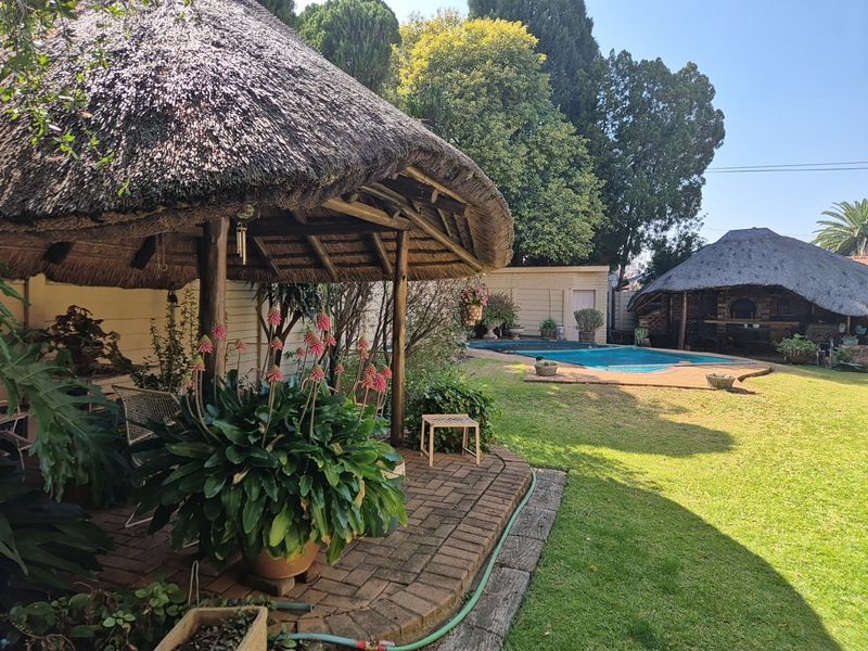 Spacious backyard featuring a swimming pool, a traditional thatch-roof lapa, brick-paved patio area, and established garden surroundings.