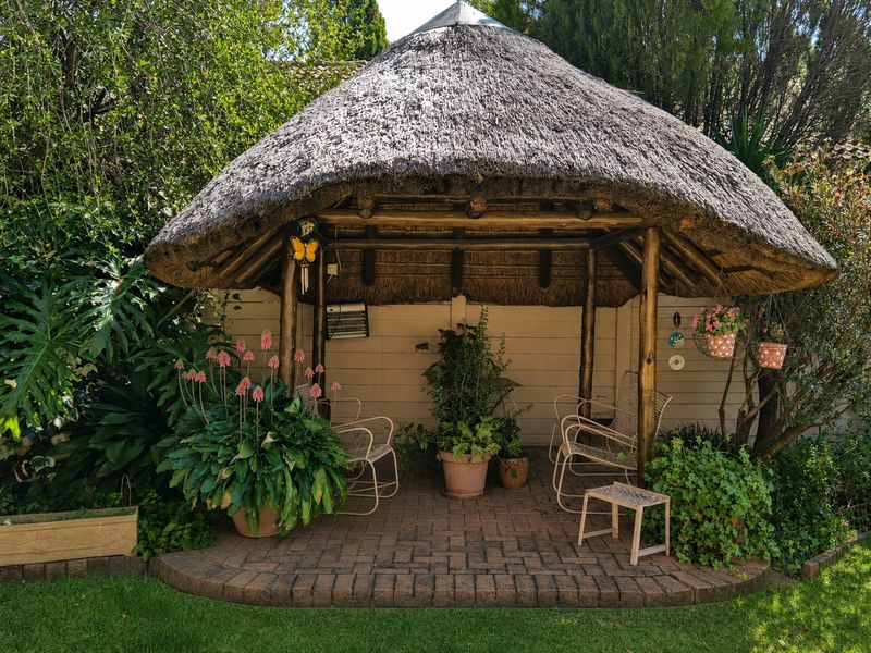 A charming outdoor thatched gazebo featuring a brick-paved patio area, providing a shaded and tranquil space within the garden.