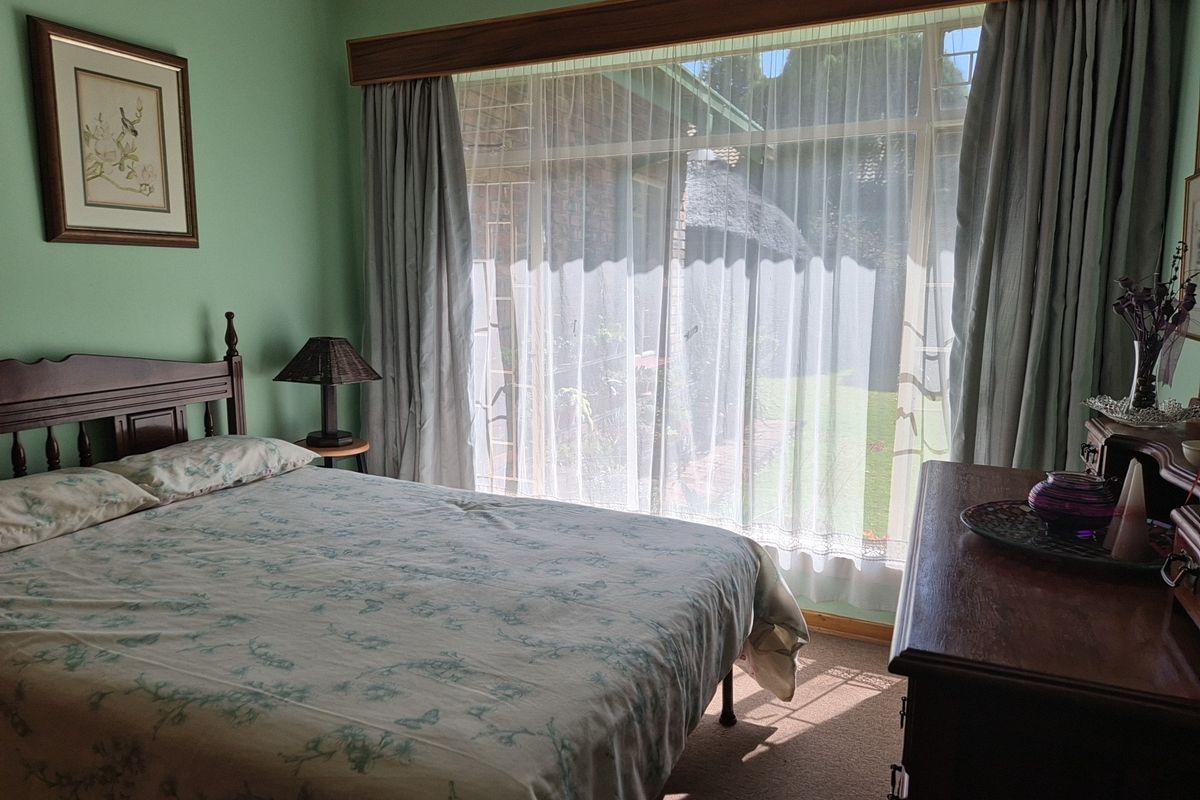 A bedroom featuring a large window with garden views, carpeted flooring, and neutral wall finishes.