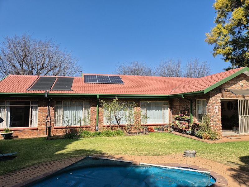 Rear view of a brick house featuring a tiled roof with solar panels, a swimming pool with cover, and a landscaped garden area.