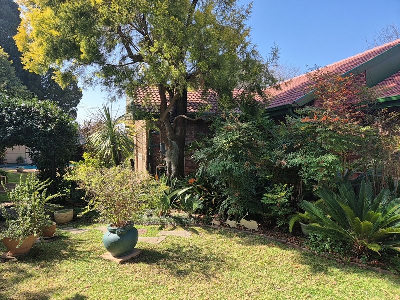 A view of the rear garden featuring established landscaping, a lawn area, and the brick facade of the house with a tiled roof.