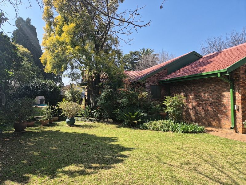 A view of the rear garden featuring a well-maintained lawn, mature trees, and the brick exterior of the house with a tiled roof.