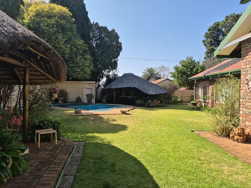 Spacious rear garden featuring a swimming pool, a traditional thatched lapa, and well-maintained lawn areas adjacent to the main house.