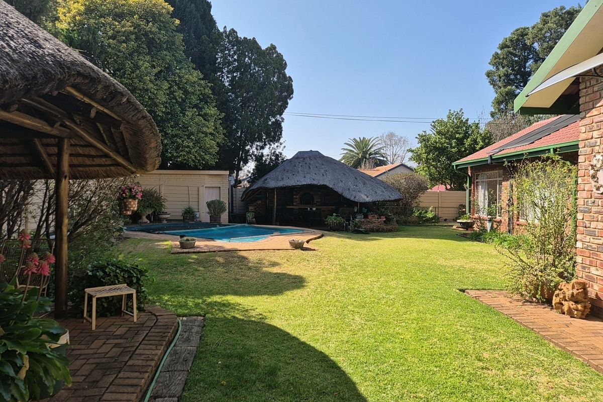 Spacious rear garden featuring a swimming pool, a traditional thatched lapa, and well-maintained lawn areas adjacent to the main house.