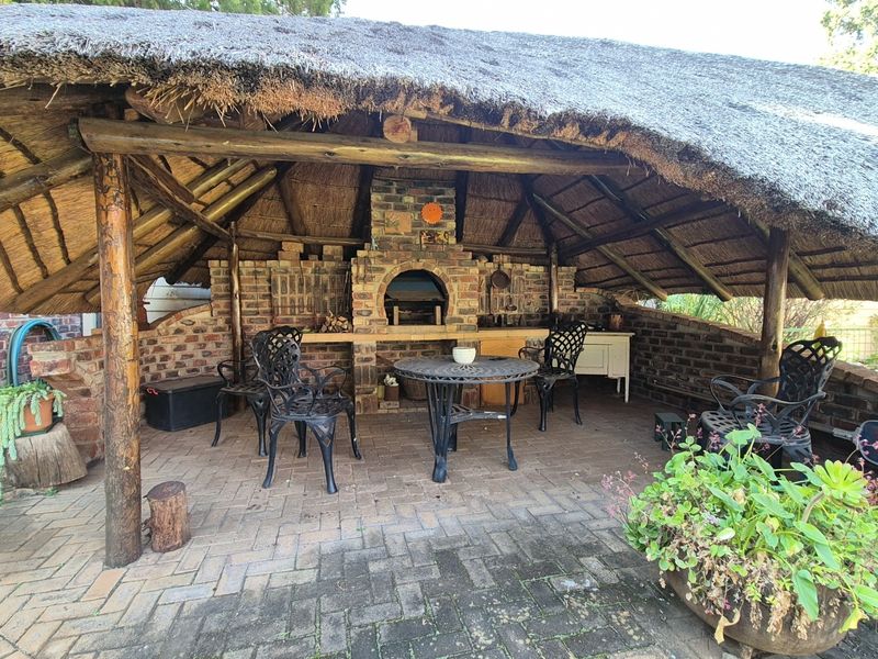 Covered outdoor patio area featuring a rustic brick fireplace, built-in pizza oven, and traditional thatched roof structure.