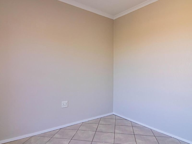 A clean, empty bedroom corner featuring neutral painted walls, tiled flooring, and standard electrical fixtures.