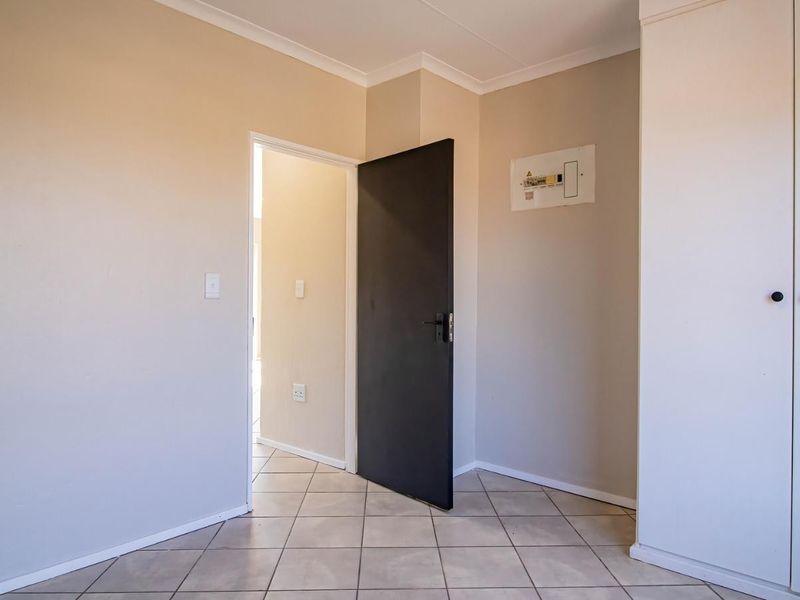 A clean, empty bedroom featuring neutral wall tones, tiled flooring, and a built-in cupboard, providing a versatile space ready for personalization.