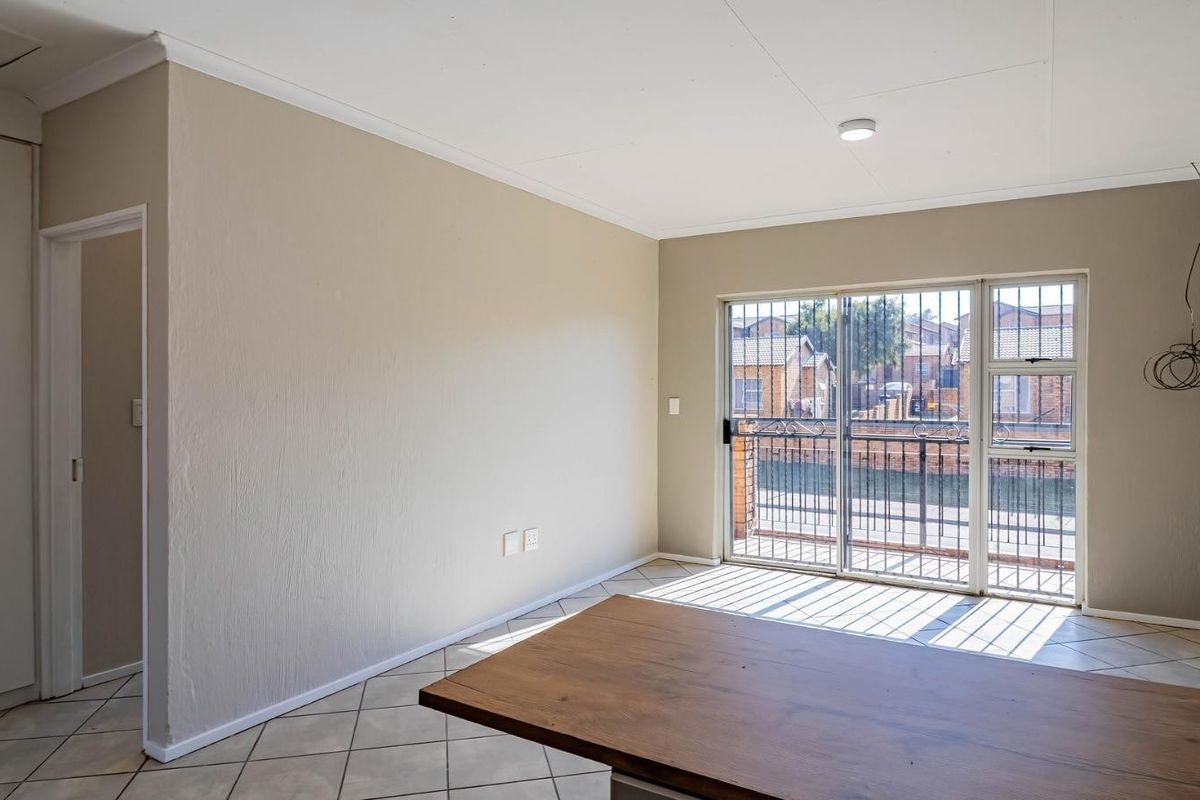 An empty living room featuring tiled floors, an exposed brick feature wall, and a sliding glass door with security gate leading to a balcony.