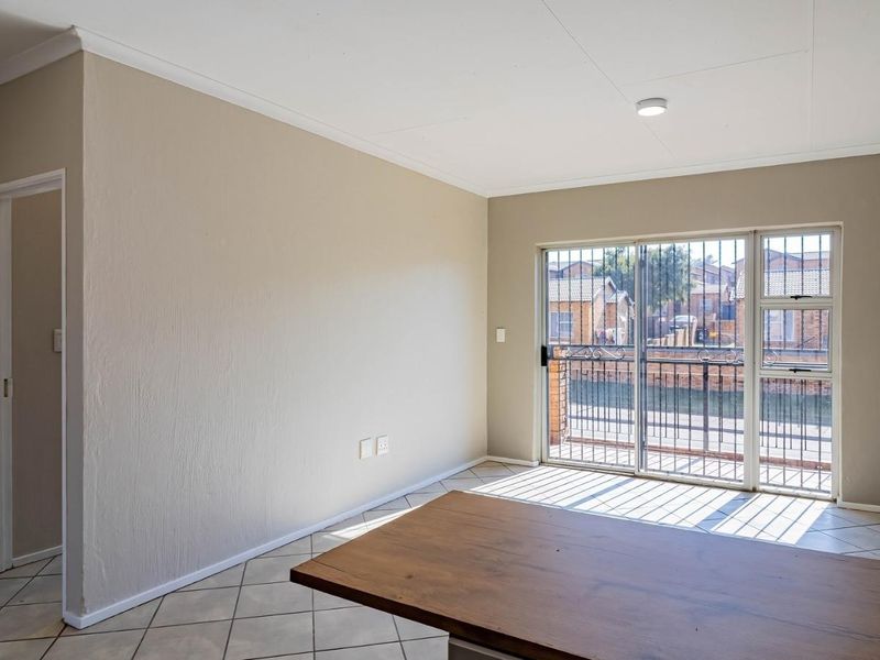 An empty living room featuring tiled floors, an exposed brick feature wall, and a sliding glass door with security gate leading to a balcony.