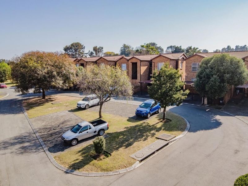 An aerial view of a residential apartment complex featuring brick facades, tiled roofs, and paved communal driveway areas with established trees.