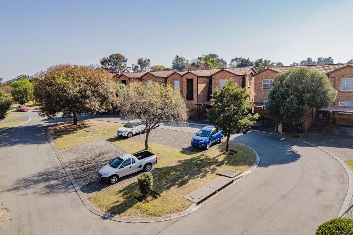 An aerial view of a residential apartment complex featuring brick facades, tiled roofs, and paved communal driveway areas with established trees.