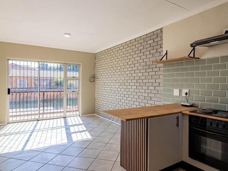 Open-plan living area featuring a modern kitchen with subway tile backsplash, built-in oven, hob, and an exposed brick feature wall leading to a balcony.