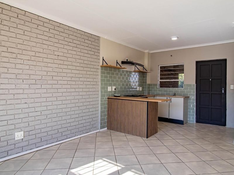 Open-plan living area featuring a modern kitchen with subway tile backsplash, wooden breakfast bar, and a distinctive grey exposed brick feature wall.
