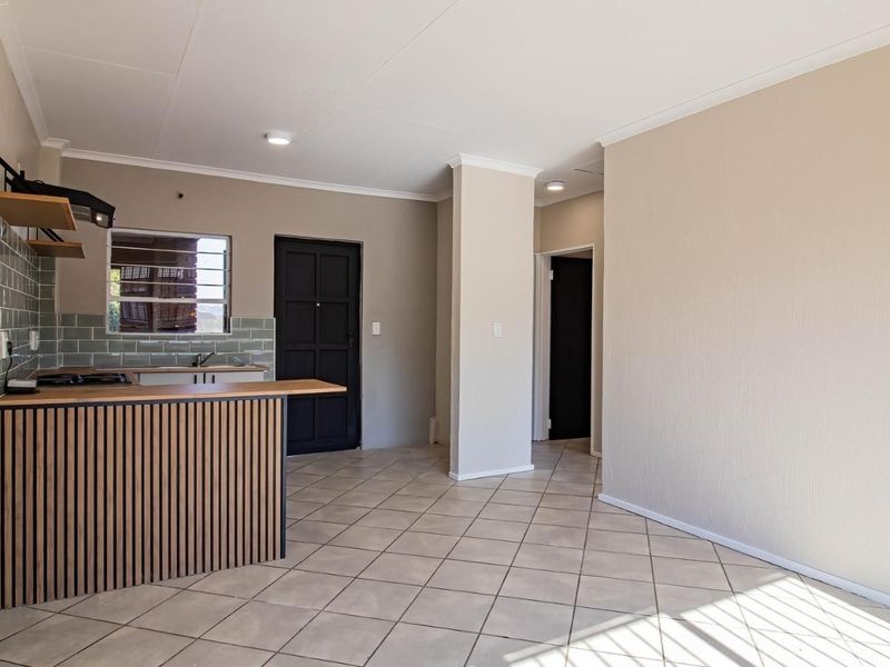 An open-plan living and kitchen area featuring tiled floors, a modern breakfast bar, subway tile backsplash, and built-in kitchen cabinetry.
