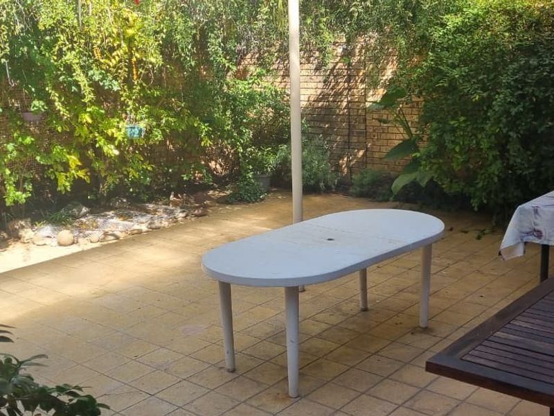 A paved outdoor patio area enclosed by brick boundary walls and established garden greenery, providing a private space for outdoor relaxation.