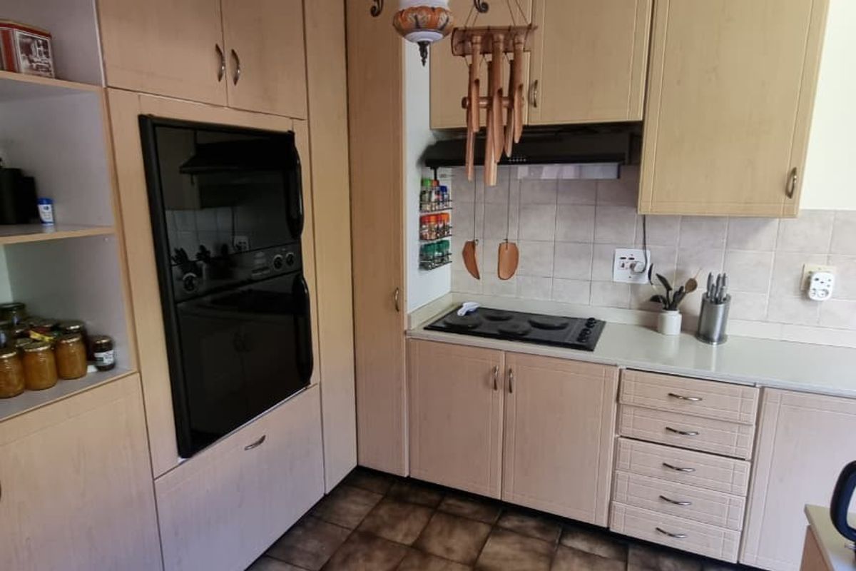 A functional kitchen featuring light wood-finish cabinetry, a built-in oven, electric hob, extractor fan, and tiled backsplash with a stainless steel sink.