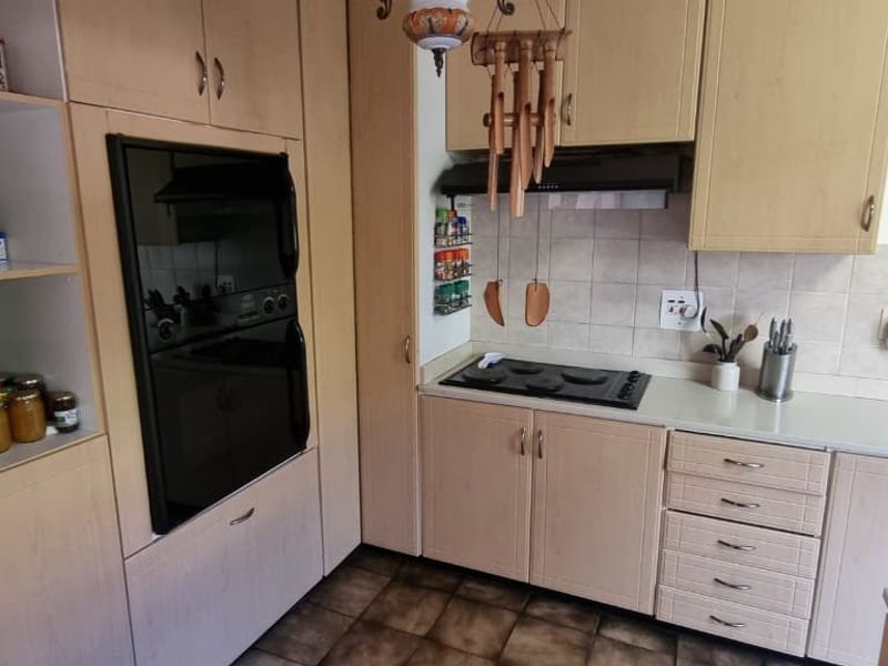 A functional kitchen featuring light wood-finish cabinetry, a built-in oven, electric hob, extractor fan, and tiled backsplash with a stainless steel sink.