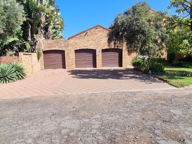 Front view of a residential property featuring a triple garage with roller doors, a paved driveway, and established garden landscaping.