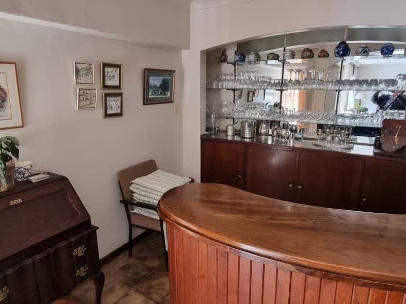 A dedicated bar area featuring a built-in wooden counter, mirrored back bar with glass shelving, and tiled flooring.