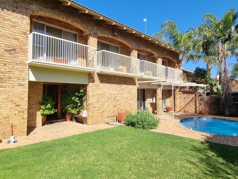 Rear view of a double-story brick house featuring a swimming pool, paved patio area, and upper-level balconies with metal railings.